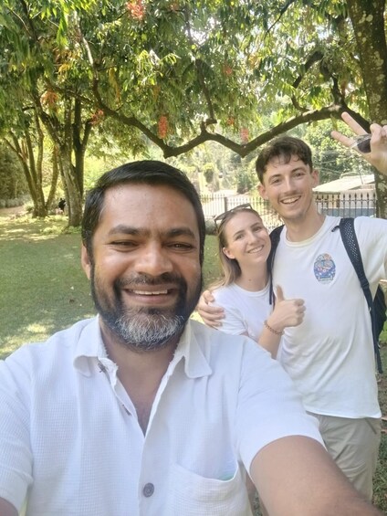 En grupp människor som tar en selfie i en park med träd och ett staket i bakgrunden. 2