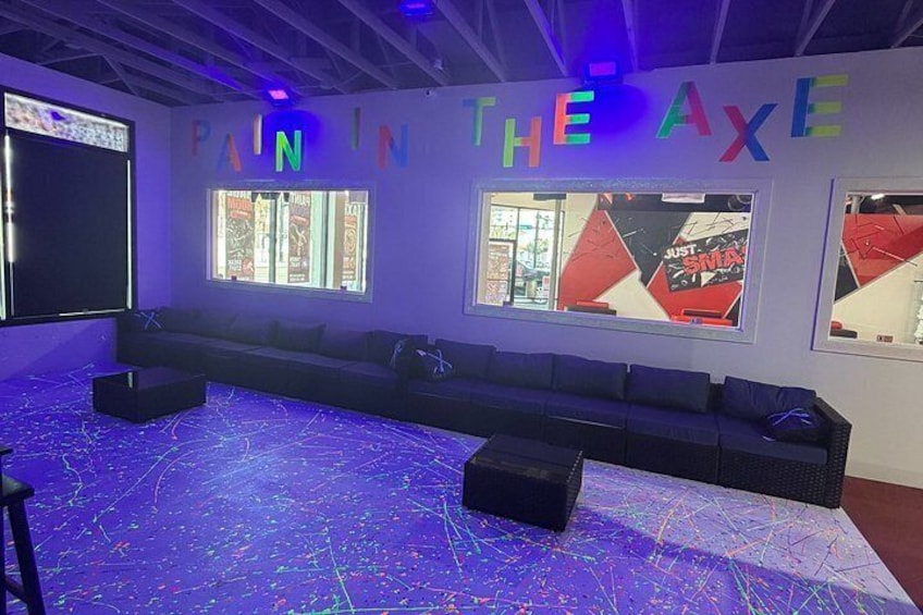 A room with a long black couch, a projector screen, and a wall with colorful letters spelling 'PAIN IN THE AXE'. 3