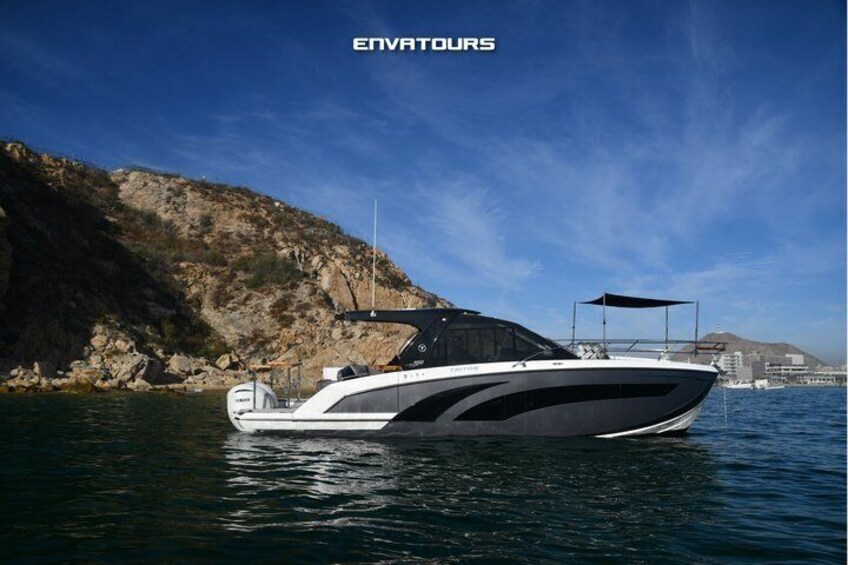 A white and black motorboat on calm water with a rocky coastline and a clear sky in the background. 5