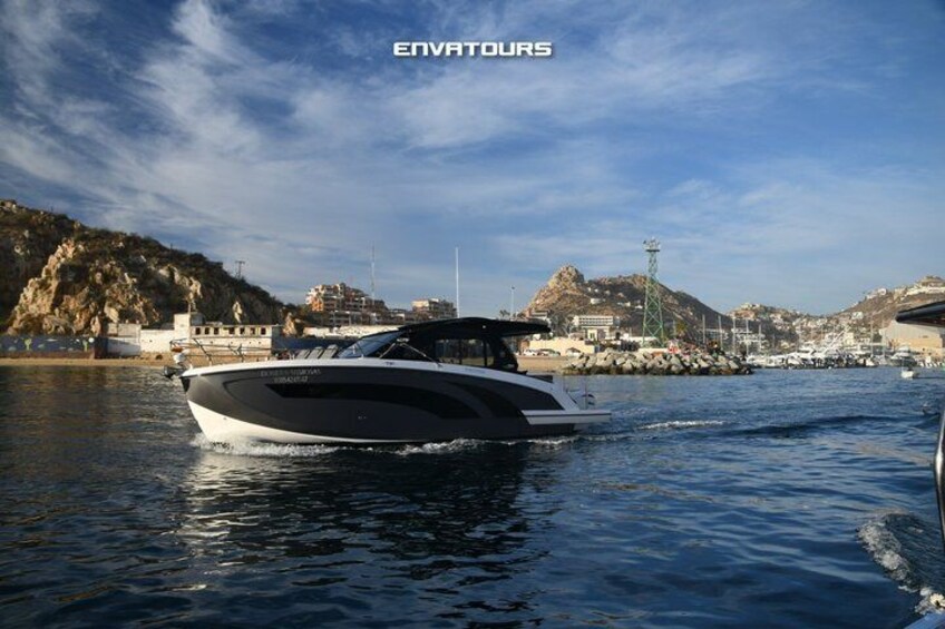 A sleek, modern yacht on calm waters with a coastal town and rocky hills in the background. 1