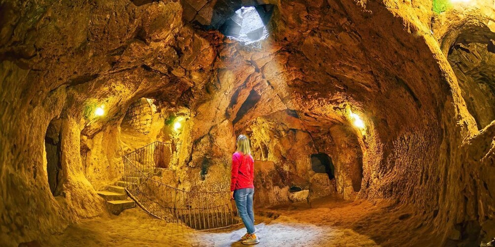 A person standing in a cave with a staircase and a light source above. 2