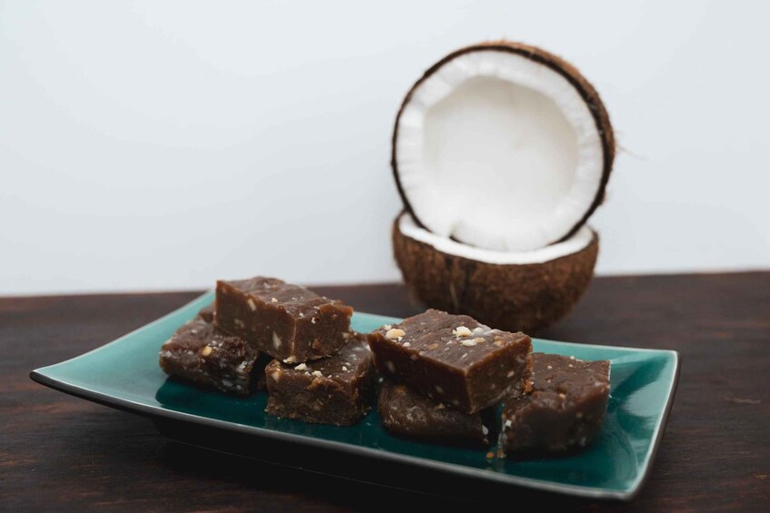 Un piatto di dolcetti scuri a base di cocco, con un intero cocco sullo sfondo. 4