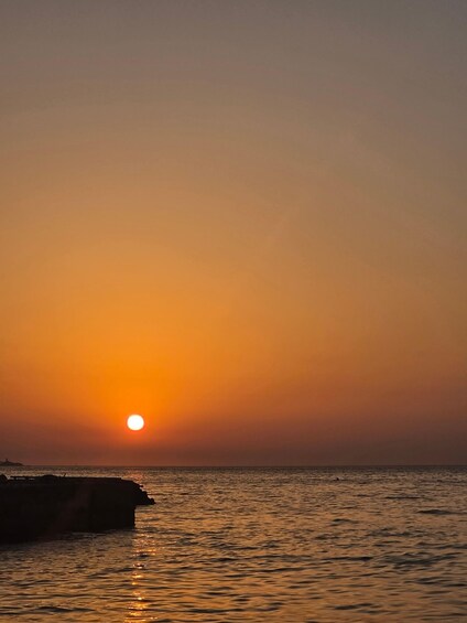 A sunset over a calm sea with a rocky outcrop in the foreground. 5