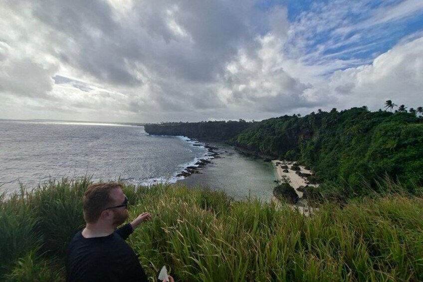 A coastal landscape with a person overlooking the sea, a beach, and a forested cliff. 3