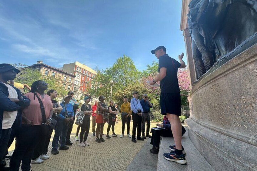 A group of people standing on steps, facing a statue. 1