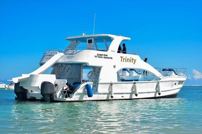A white boat named Trinity with a cabin and a motor, floating on calm water. 5
