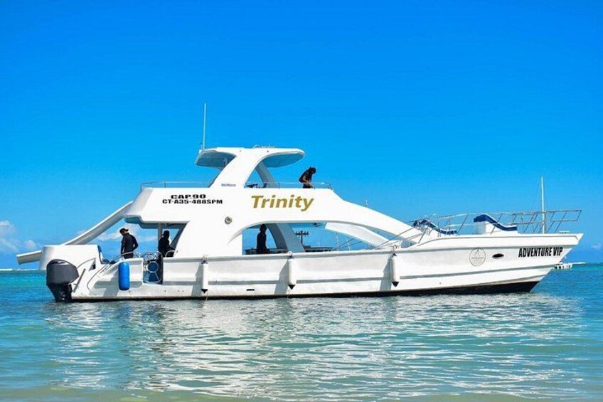 A white yacht named 'Trinity' with 'Adventure VIP' written on the side, docked in calm waters. 3