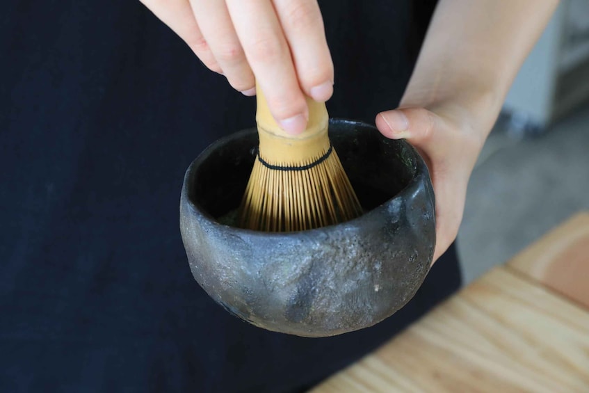A person holding a whisk in a ceramic bowl. 1