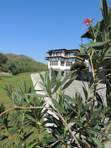 A two-story house with a balcony, surrounded by greenery and a clear blue sky. 1