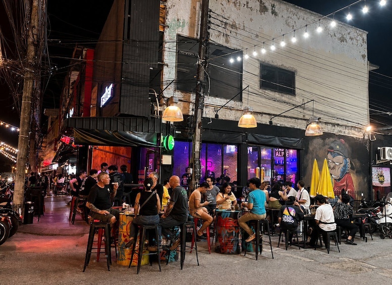A bustling street scene at night with people dining at outdoor tables, illuminated by string lights and hanging lamps. 2