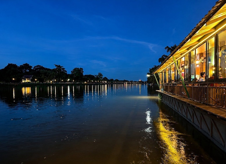 A calm lake at dusk with a docked boat and a building with illuminated windows. 1