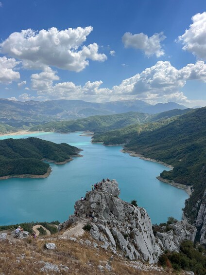 A mountainous landscape with a turquoise lake surrounded by greenery and a rocky peak in the foreground. 5