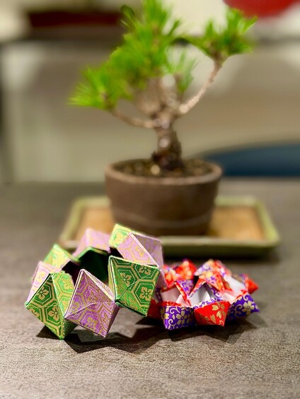 A bonsai tree in a brown pot on a table with colorful origami figures. 2