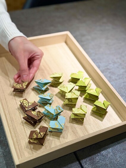 A hand arranging colorful paper blocks on a wooden tray. 4