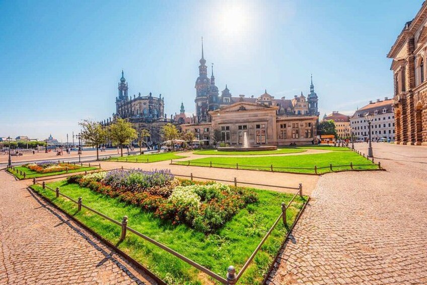 A cobblestone square with a central garden, historic buildings, and a prominent church tower. 3