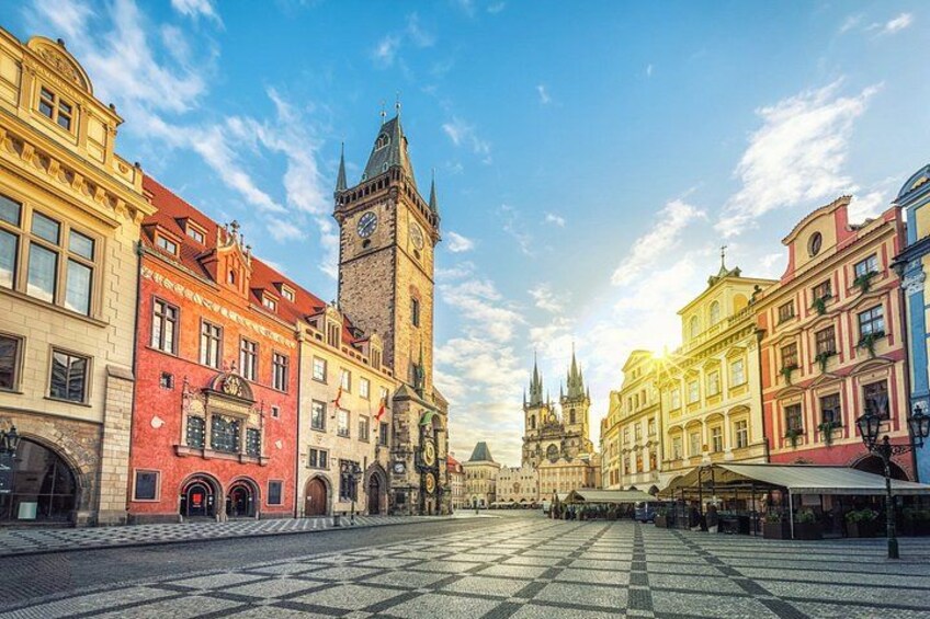 A historic square with a prominent clock tower, colorful buildings, and cobblestone pavement. 2