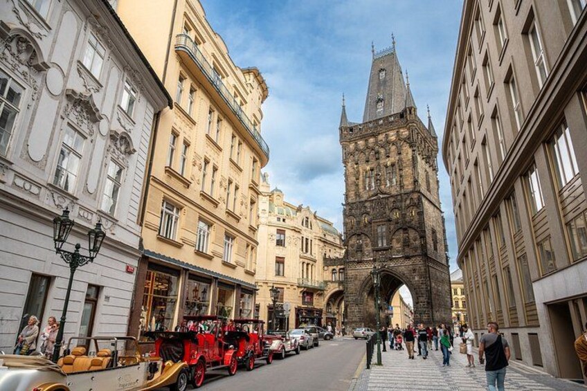 A historic street with a prominent tower, pedestrians, and vintage cars. 4
