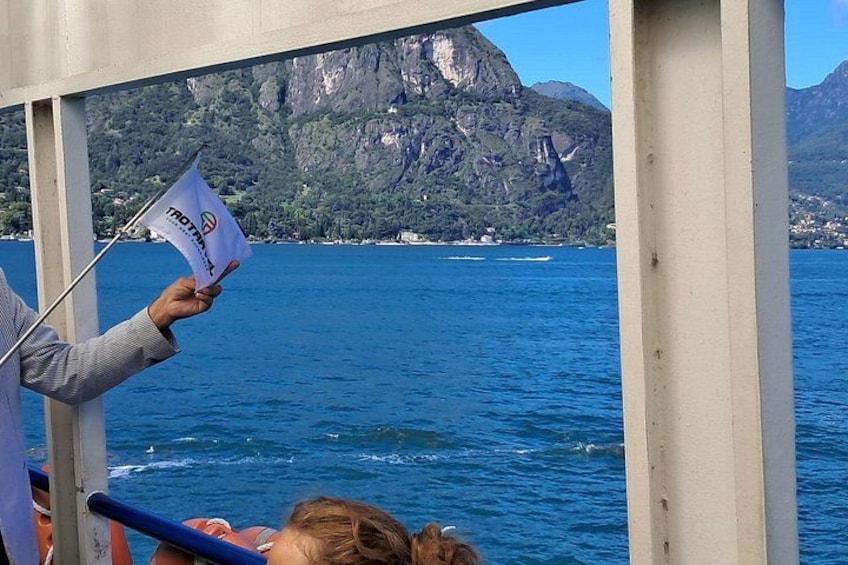 A person holding a flag with text on a boat, with a mountainous landscape in the background. 3