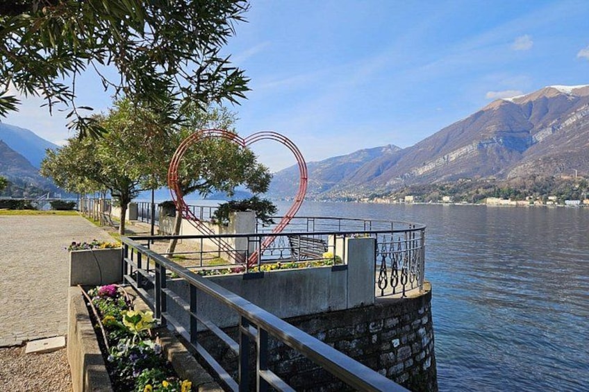 A lakeside walkway with a heart-shaped sculpture, a bridge in the background, and mountains. 2