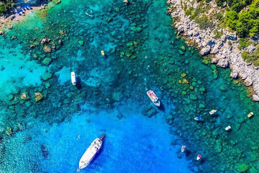 A clear blue sea with boats anchored near a rocky shore. 2