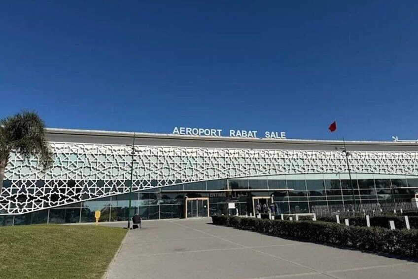 An airport terminal with a modern facade, a clear sky, and a flag on top. 1