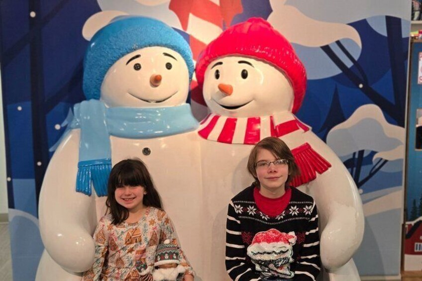 Two people standing in front of a snowman decoration. 2