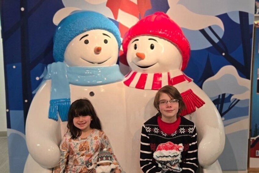 Two children sitting in front of a snowman decoration. 3