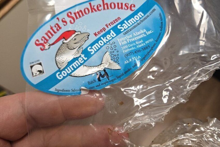 A hand holding a package of Gourmet Smoked Salmon from Santa's Smokehouse. 4