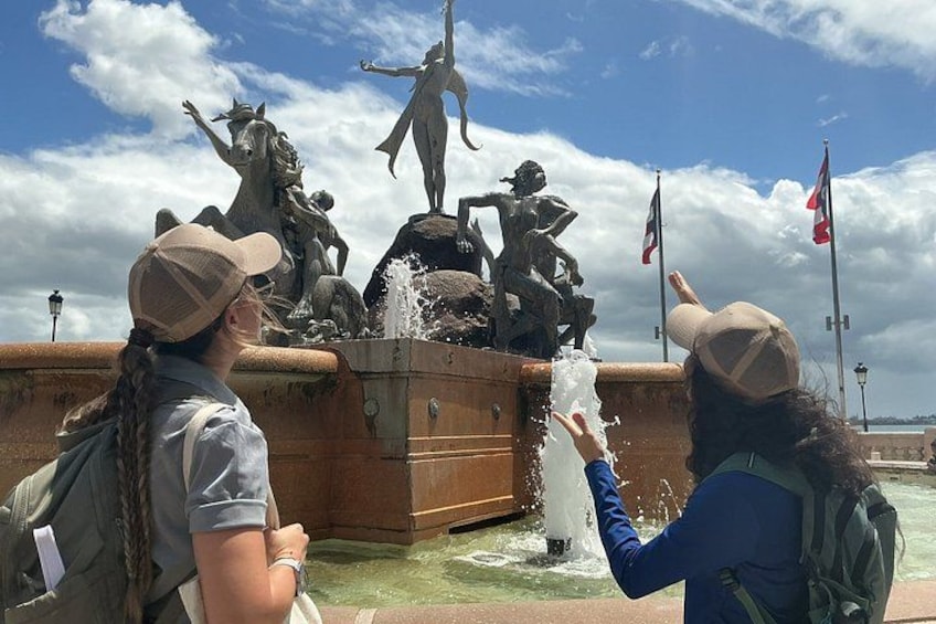 A fountain with statues and water spouts, surrounded by a stone wall and flags. 4