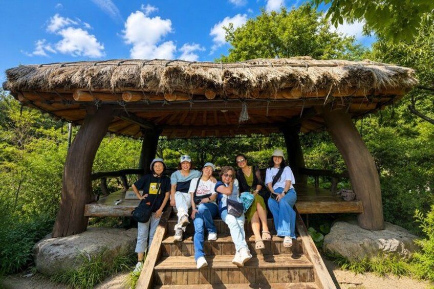 A group of people sitting on wooden steps under a thatched structure in a forested area. 5