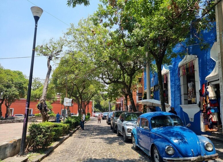 A cobblestone street lined with trees and vintage cars, with a blue building on the right. 2