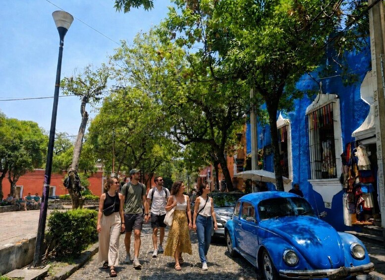A cobblestone street lined with trees and a blue vintage car parked on the side. 1
