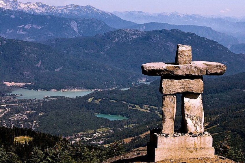 A stone cross in a mountainous landscape with a lake and forested area in the background. 2