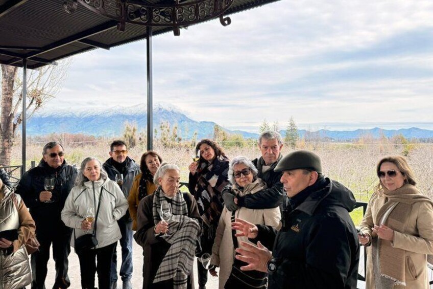 A group of people standing outdoors, some holding glasses, with a mountainous landscape in the background. 5