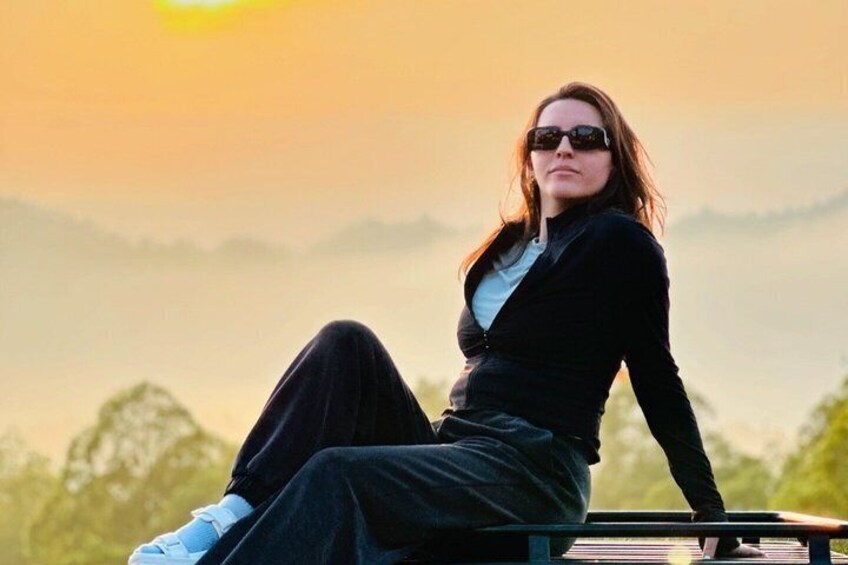 A person sitting on a bench with a sunset in the background. 1