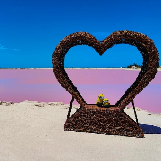 A heart-shaped sculpture on a beach with a clear blue sky and pink water. 5
