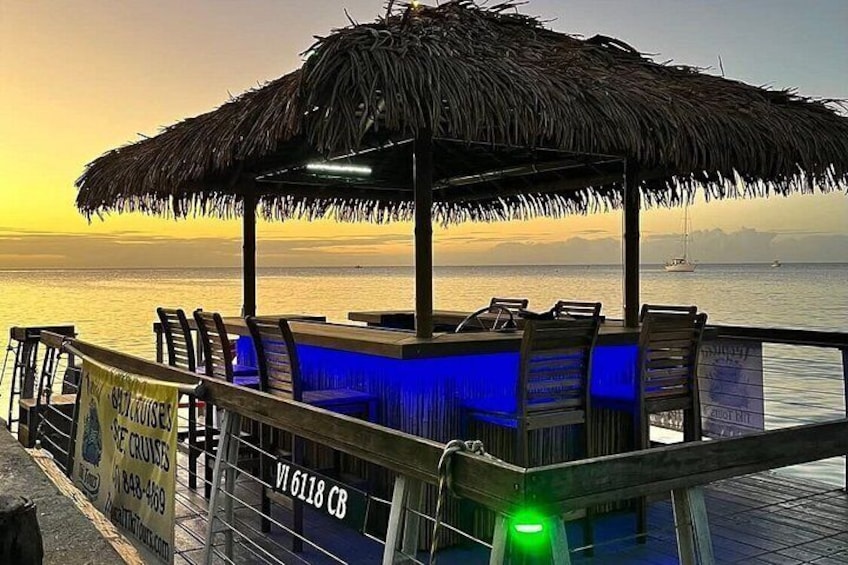 A beach bar with a thatched roof, wooden chairs, and a view of the ocean at sunset. 3