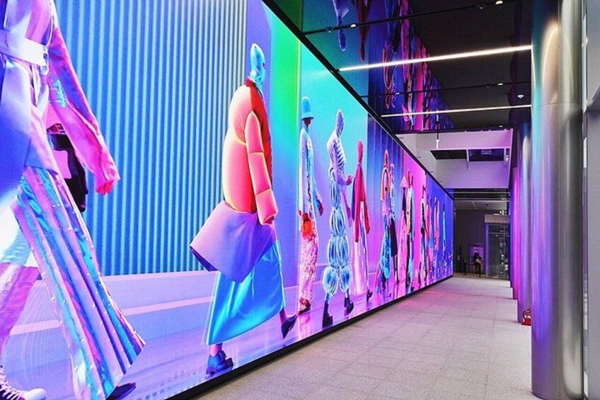 A modern indoor space with a large digital display featuring mannequins in various outfits. 5