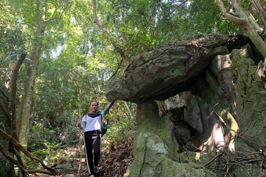 A person standing next to a large rock formation in a forest. 1