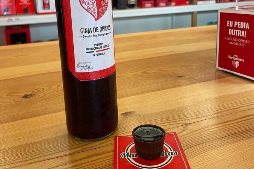 A bottle of Ginja de Obidos wine with a red label, a glass of wine, and a red coaster with the brand name. 4