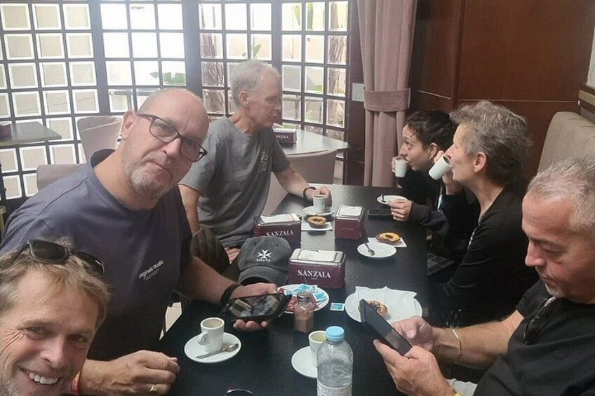 A group of people sitting around a table with coffee cups, a water bottle, and a box labeled 'Sanzala.' 5