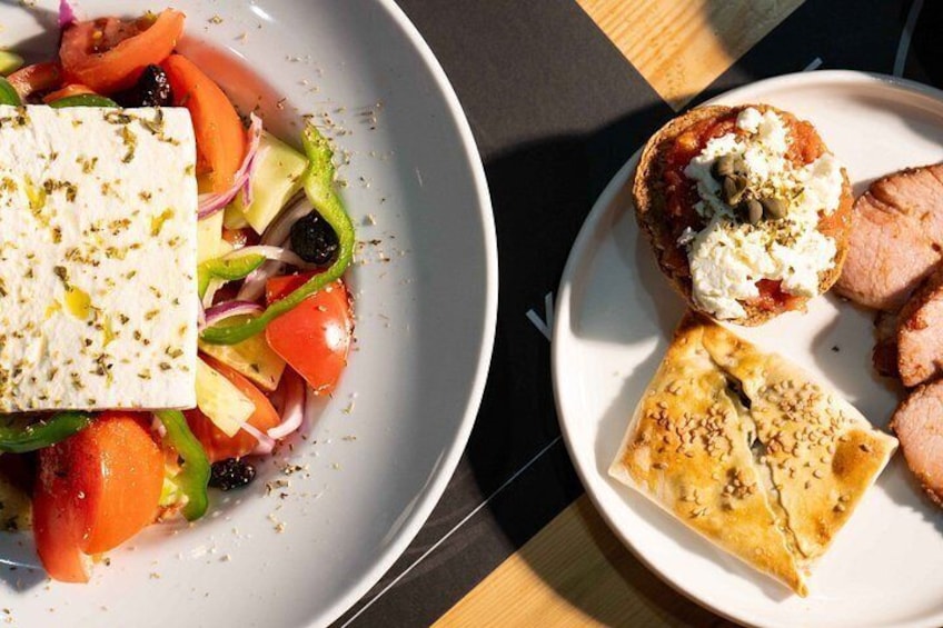 Two plates of food, one with a salad and feta cheese, the other with meat and bread. 4