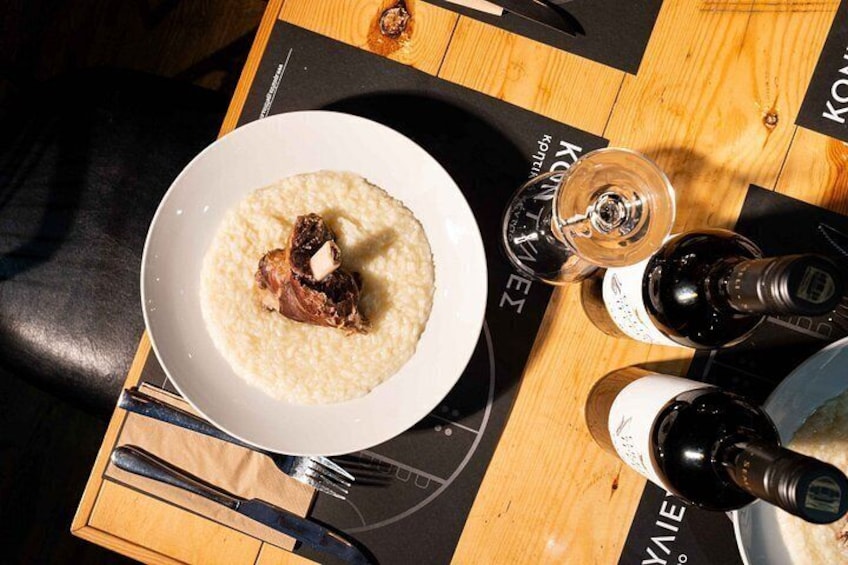 A bowl of food with a bone, a wine glass, and bottles on a table. 2