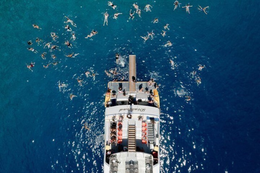 A ship with people swimming in the ocean around it. 4
