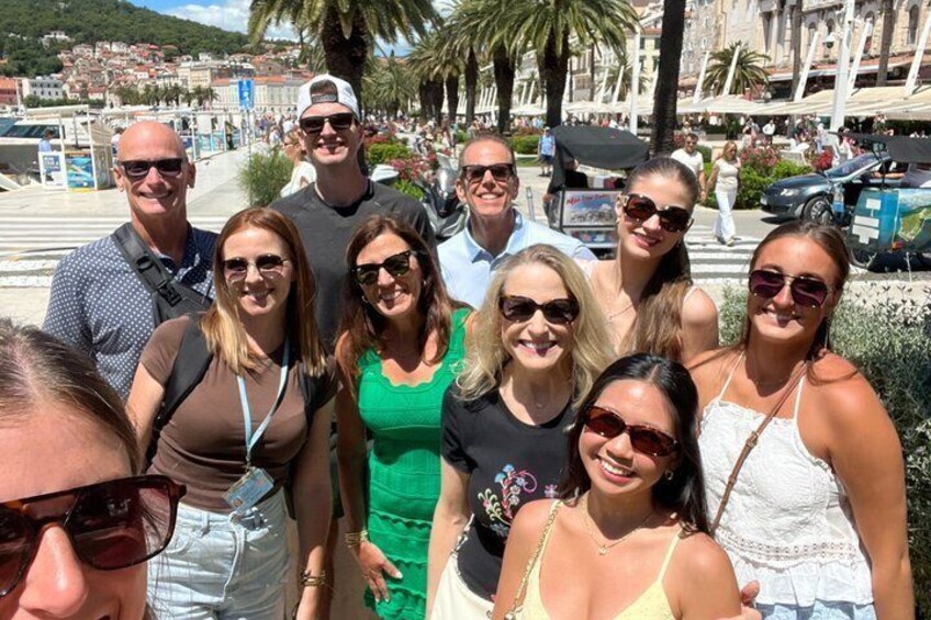 A group of people posing on a sunny promenade with palm trees and buildings in the background. 2