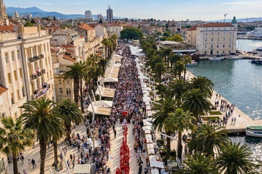 A crowded waterfront promenade lined with palm trees and buildings. 5