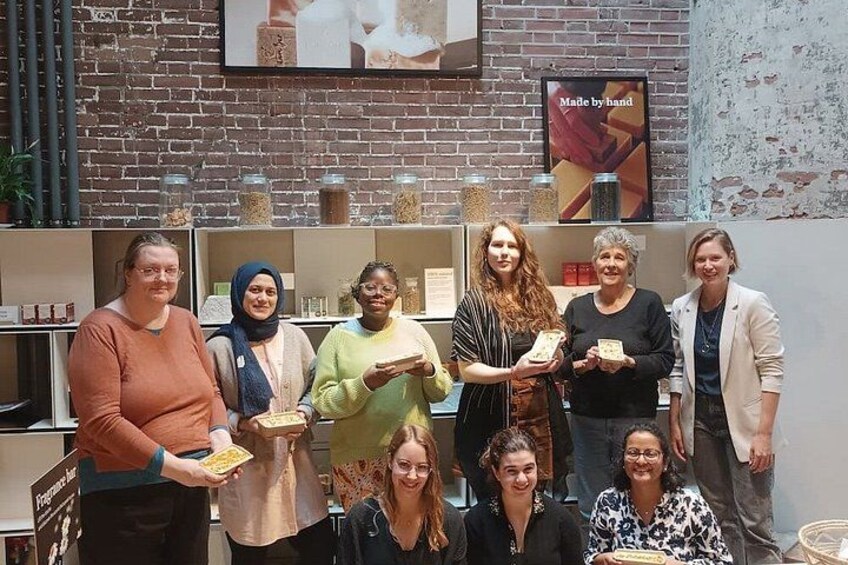 A group of people in a room with brick walls, shelves with jars, and a poster that says 'Made by hand'. 4