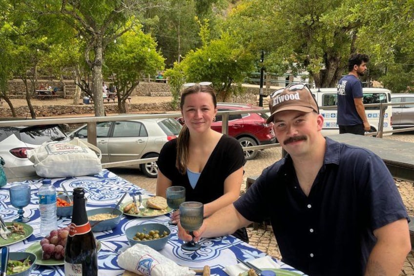 Two people sitting at an outdoor table with food and drinks. 4