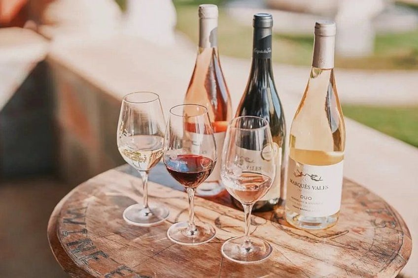 A wooden table with four wine glasses and three wine bottles. 1