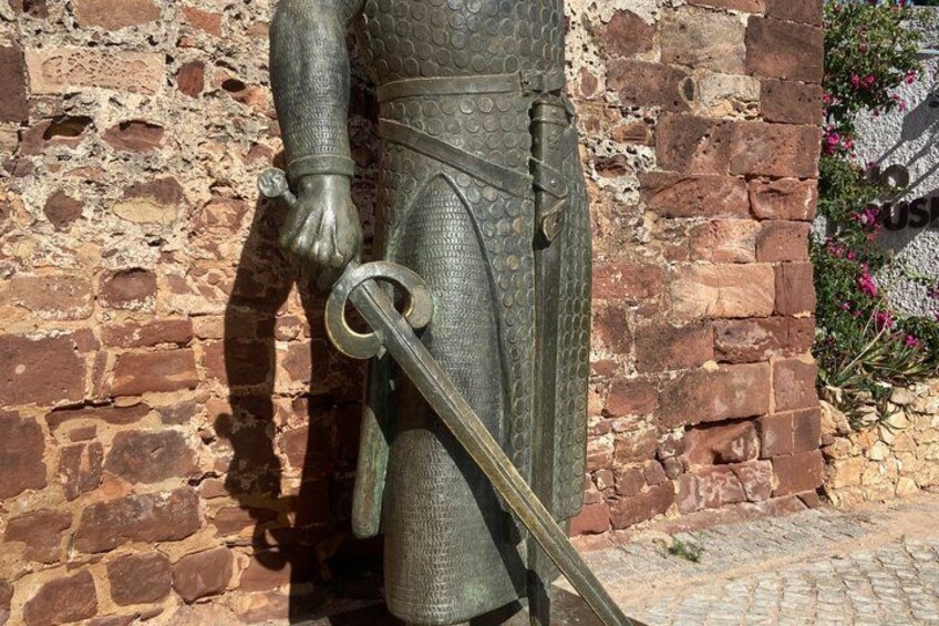 A statue of a knight in armor holding a sword, standing against a brick wall. 3